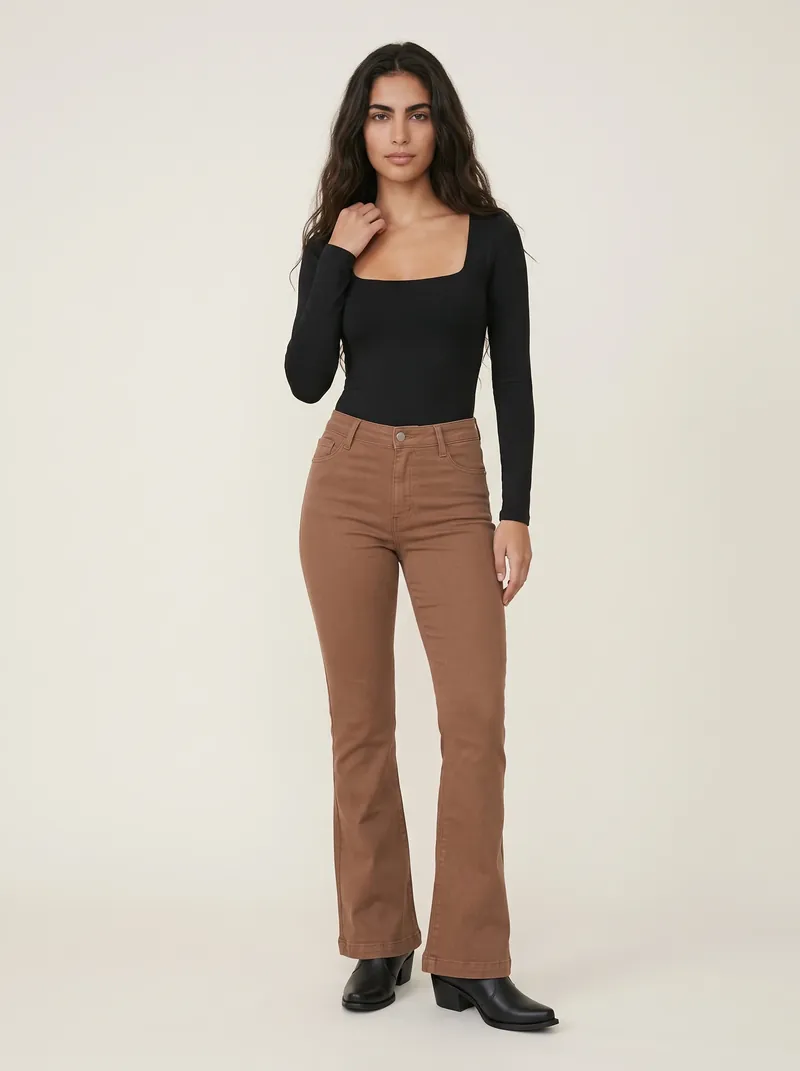 Mulher de cabelo longo ondulado com body preto de manga longa e decote quadrado, calça jeans flare marrom-caramelo de cintura alta e bota texana preta, em estúdio de fundo claro